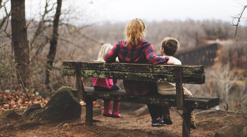 Frau sitzt mit zwei Kindern auf einer Bank im Wald.