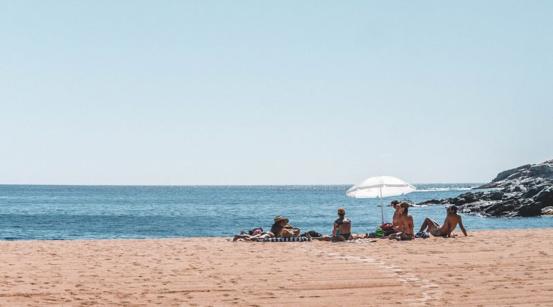 Menschen sitzen am einem Sandstrand, blaues Meer und blauer Himmel