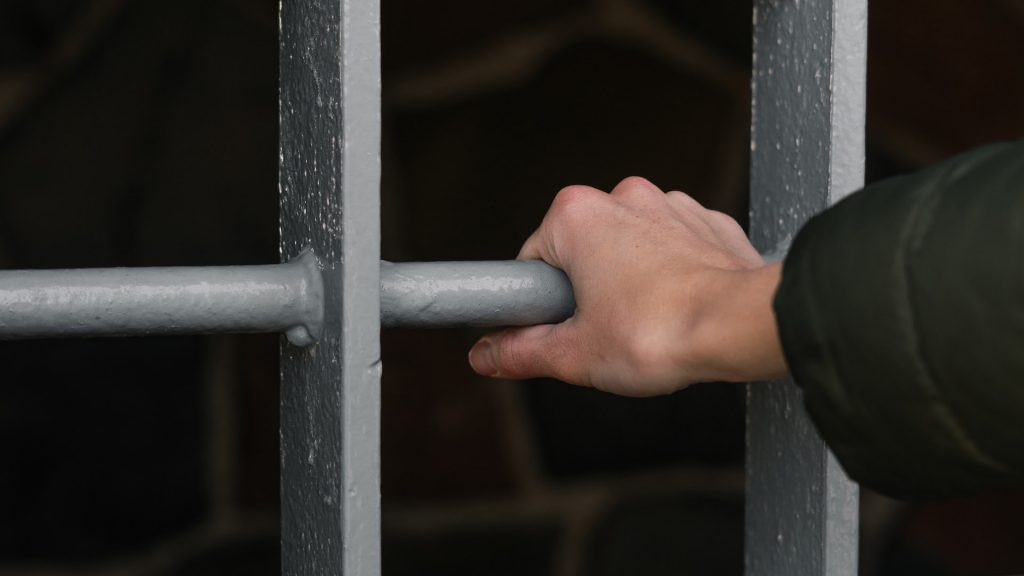 Hand hält sich an Gefängnisgitter fest