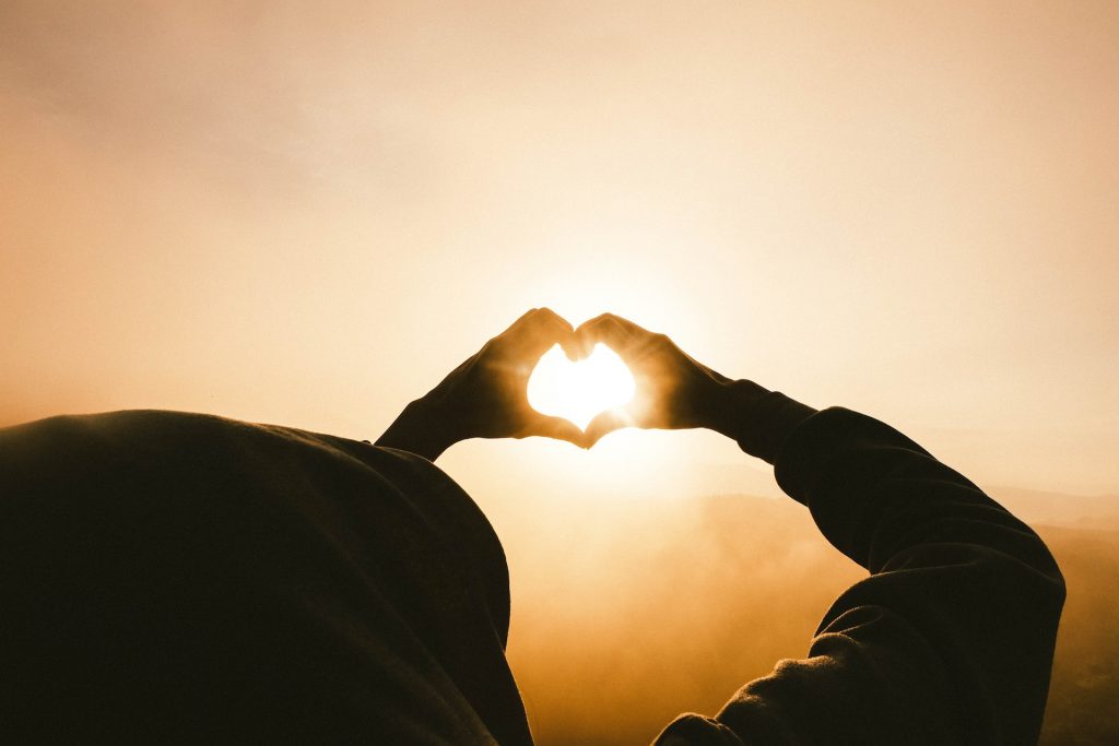 Silhouette einer Person zu Sonnenuntergang, die ein Herz mit ihren Händen formt