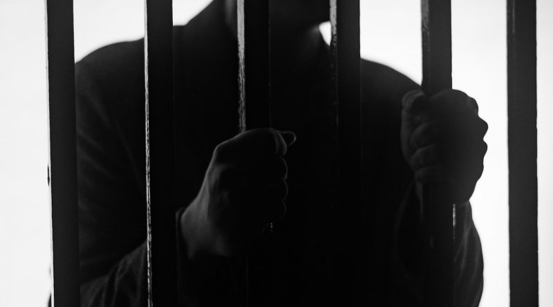 Silhouette eines Mannes, der sich mit beiden Händen an Gefängnis-Gitterstäben festhält