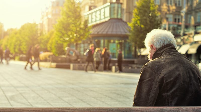Alter Mann von seitlich hinten fotografiert, wie er auf einer Bank sitzt