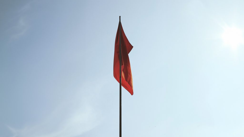 Rote Flagge, die schlaff an einem Master herunterhängt