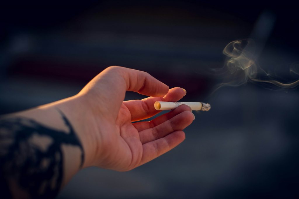 Foto einer Hand, die eine rauchende Zigarette hält