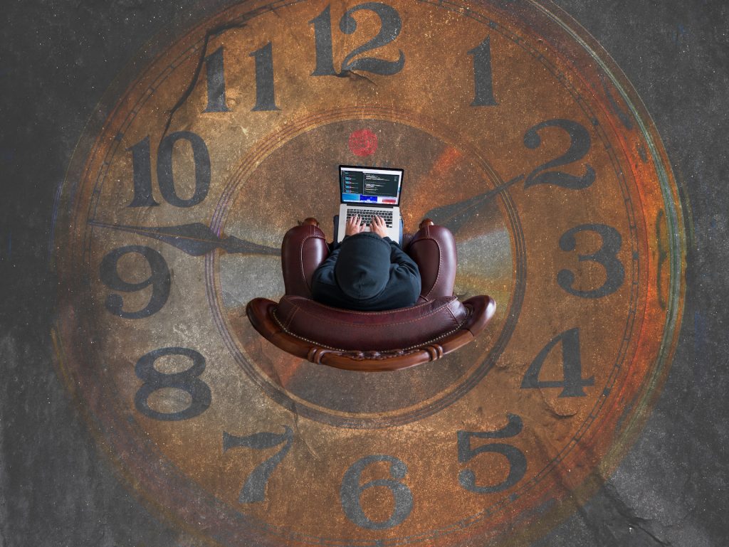 Mann mit Laptop sitzt auf einem Stuhl inmitten einer großen Uhr, von oben fotgrafiert