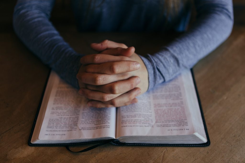 Person betet mit gefalteten Händern über einer Bibel