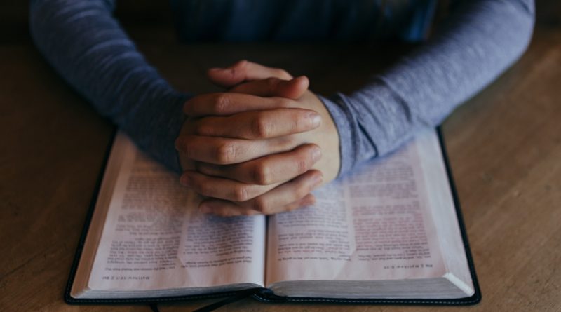 Person betet mit gefalteten Händern über einer Bibel