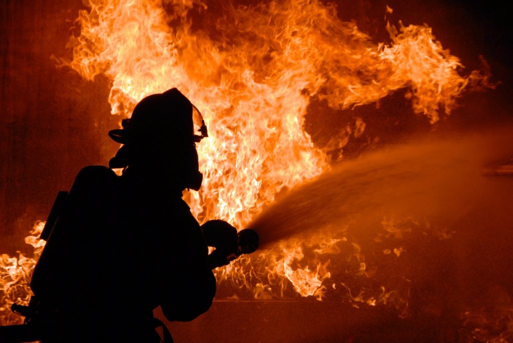 Silhouette eines Feuerwehrmannes beim Feuerlöschen, im Hintergrund Flammen
