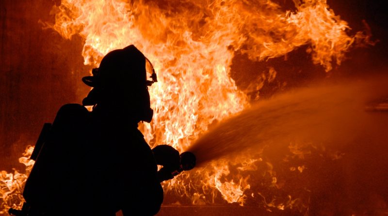 Silhouette eines Feuerwehrmannes beim Feuerlöschen, im Hintergrund Flammen