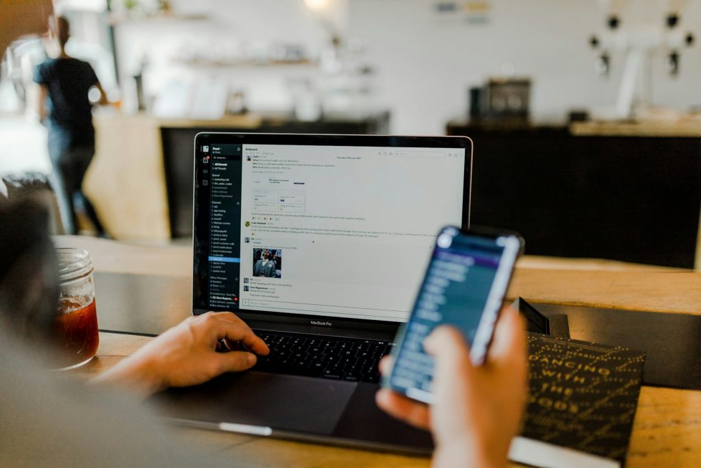 Person mit Smartphone und offenem Laptop sitzt in einem Café
