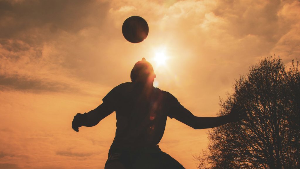 Silhouette eines Fußballers, der den Ball bei Sonnenuntergang mit dem Kopf spielt