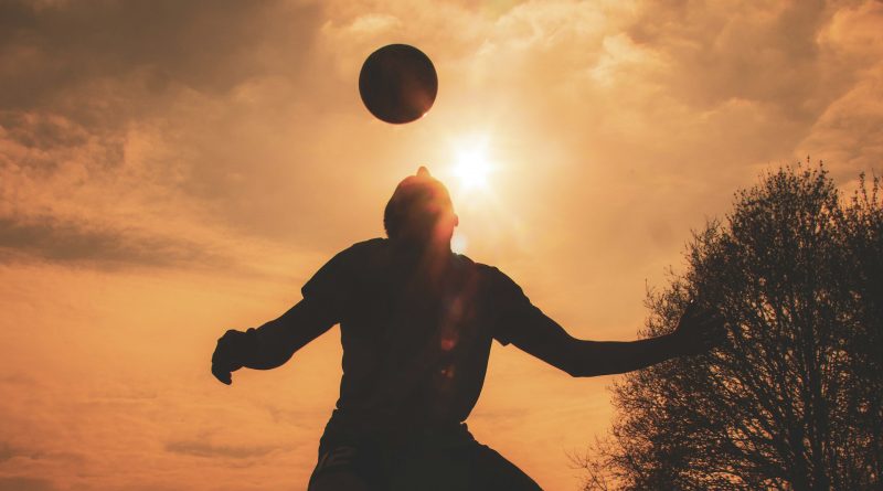 Silhouette eines Fußballers, der den Ball bei Sonnenuntergang mit dem Kopf spielt