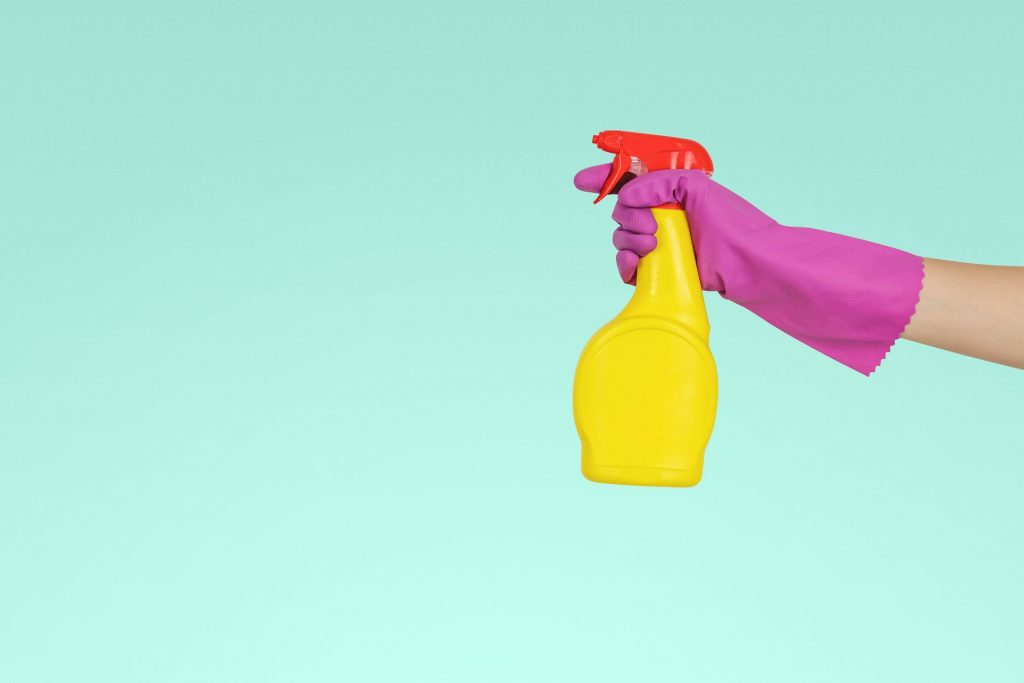 Hand mit blauem Putzhandschuh, die eine gelbe Sprühflasche hält