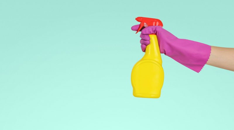 Hand mit blauem Putzhandschuh, die eine gelbe Sprühflasche hält