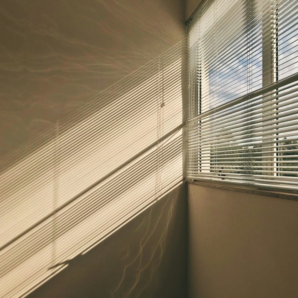 Fenster in einer Wohnung, durch den Rolladen kommen Lichtstrahlen ins Innere