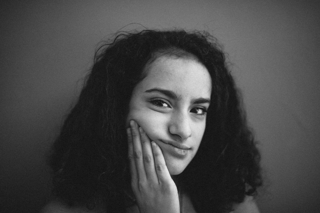 Schwarz-weiß-Foto einer Frau mit dunklen Haaren, die sich auf eine Hand stützt und gelangweilt in die Kamera blickt