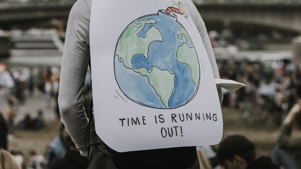Person trägt Schild mit der Aufschrift "Time is running out" und einem Bild einer Erdkugel mit Zündschnur.