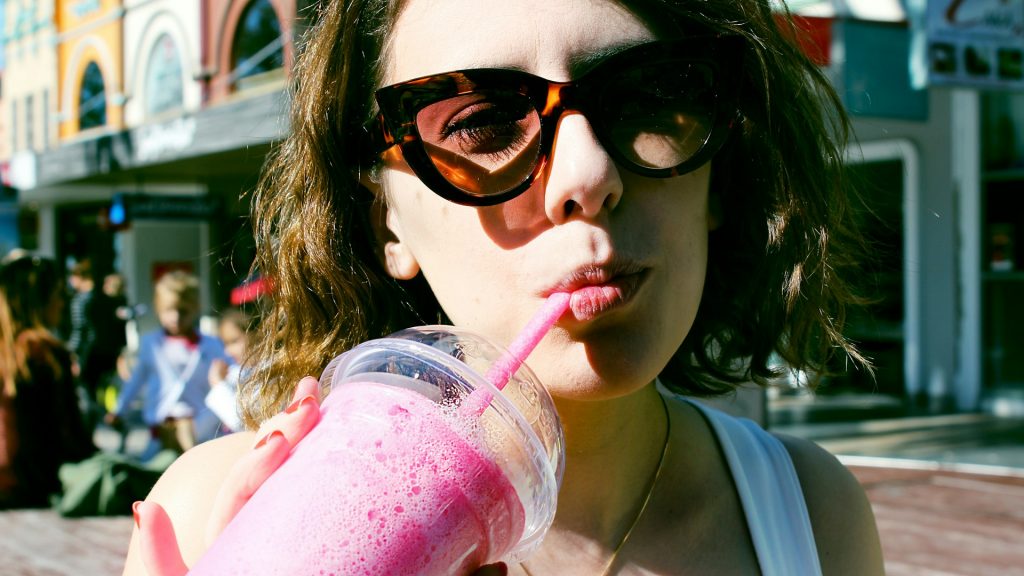 Junge Frau mit Sonnenbrille trinkt mit Strohhalm aus Becher