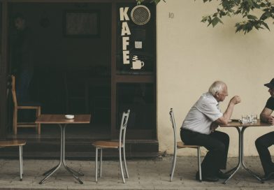 Zwei Männer sitzen an einem kleinen Tisch im Außenbereichs eines Cafés unter unterhalten sich.