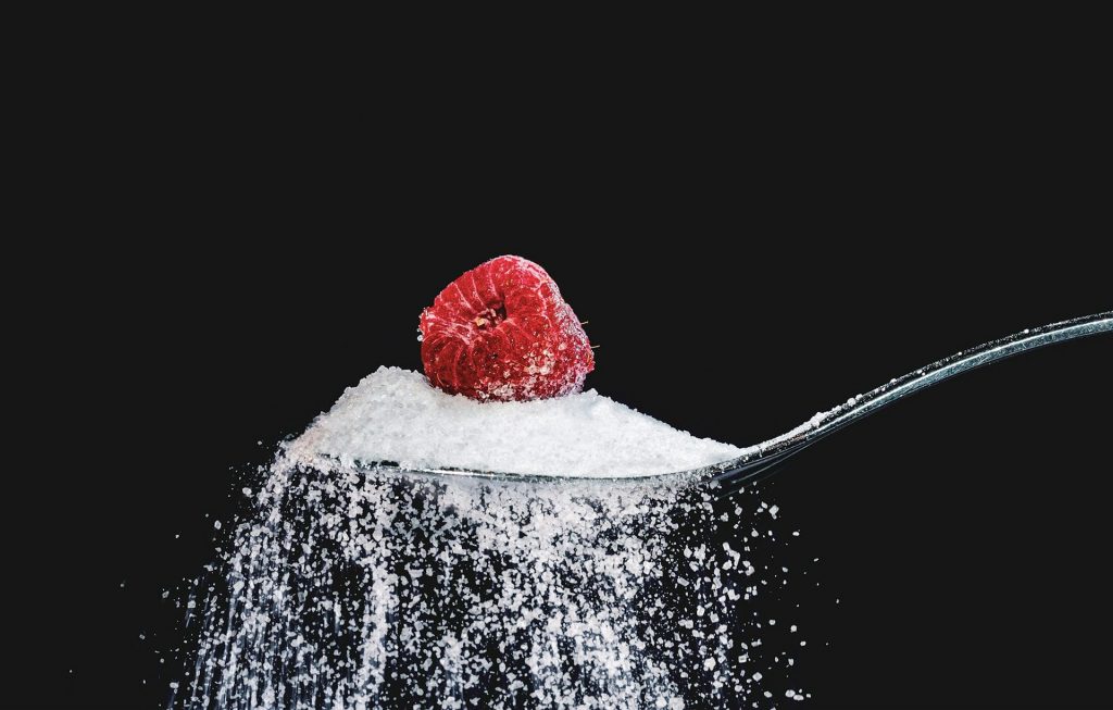 Ein Löffen Zucker, auf dem eine Himbeere liegt