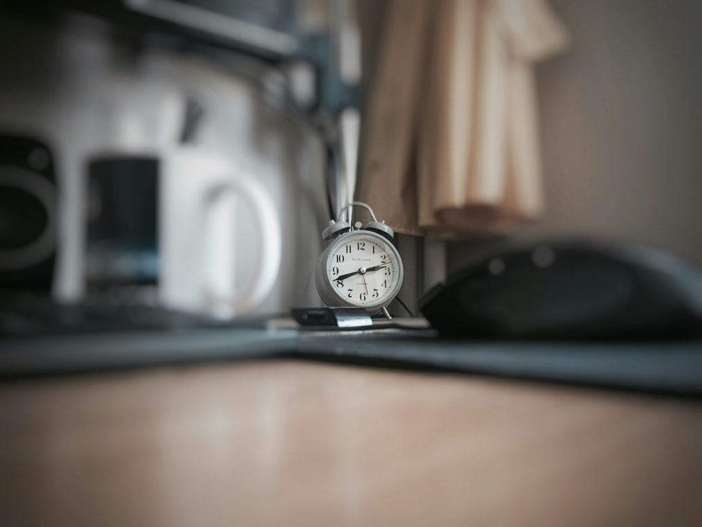 Eine analoge Uhr steht auf einem Schreibtisch mit Maus und Computer
