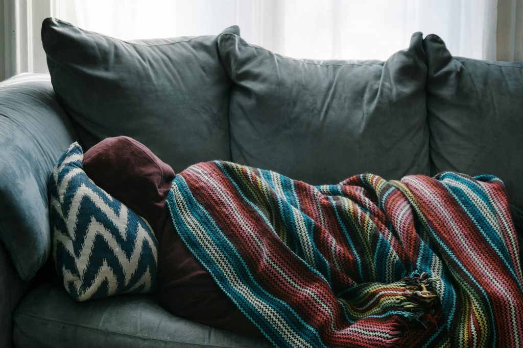 Person liegt in Decke eingewickelt auf der Couch