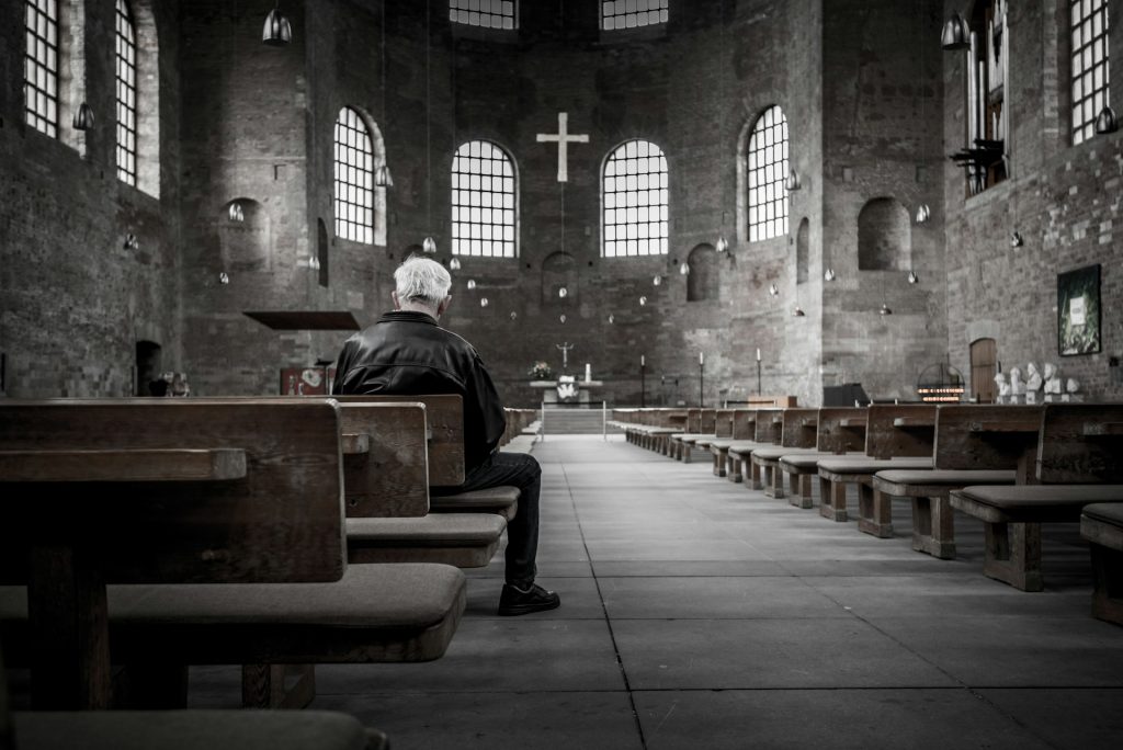 Älterer Mann sitzt alleine in einer Kirche.